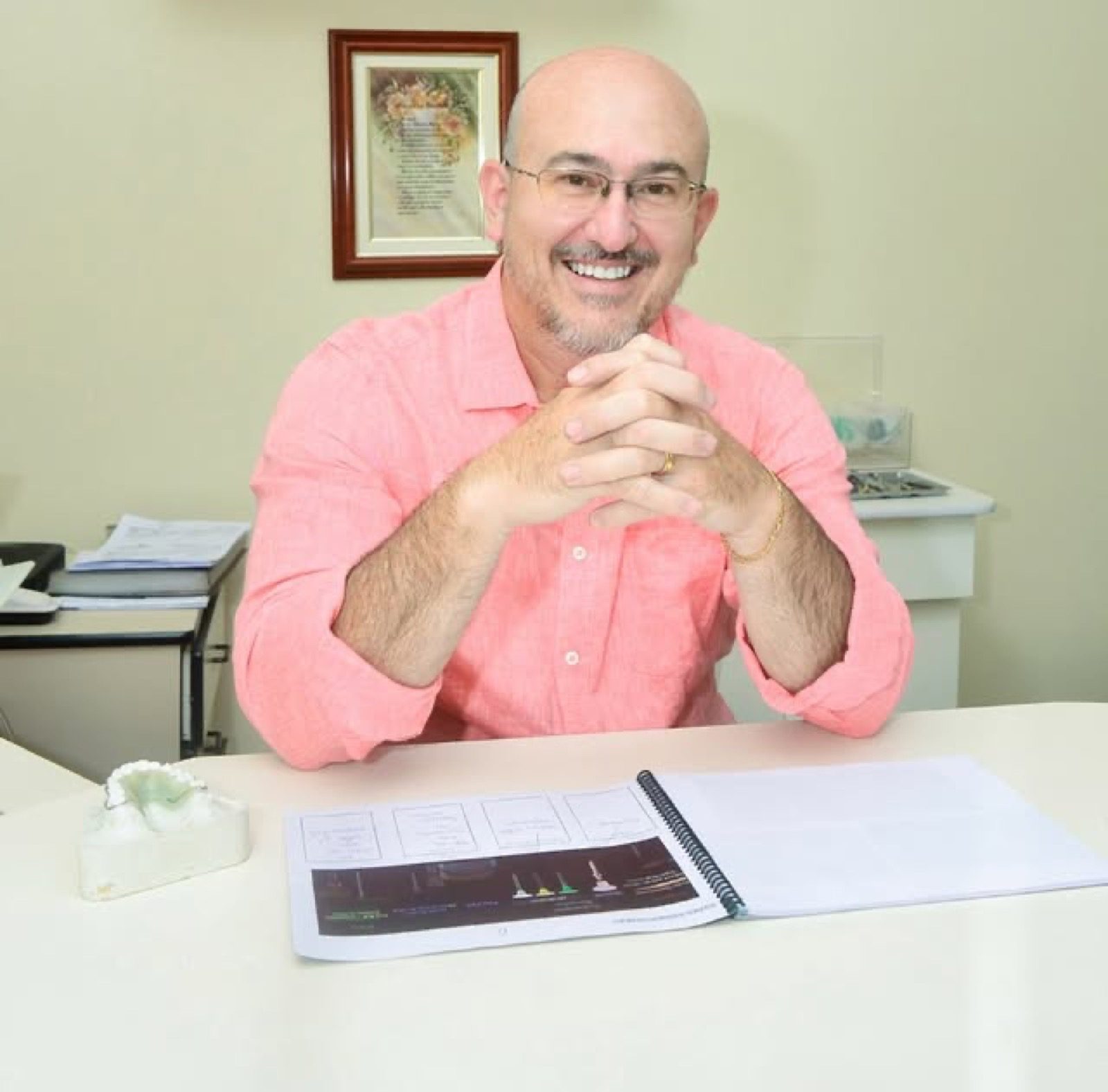 Dentista da Clínica Santini sorrindo em seu consultório, com molde odontológico sobre a mesa